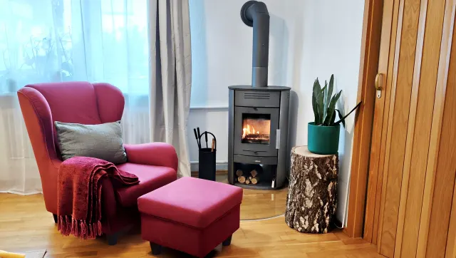 BookNoFees: alojamiento vacacional en Bensheim – Sala con estufa de leña, sillón rosa y mesita auxiliar hecha de un tocón de árbol
