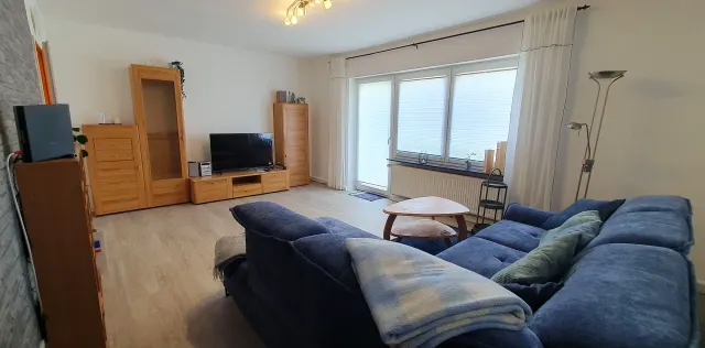 BookNoFees: alojamiento vacacional en Langelsheim – Sala con sofá azul, muebles de madera y puerta que da al balcón
